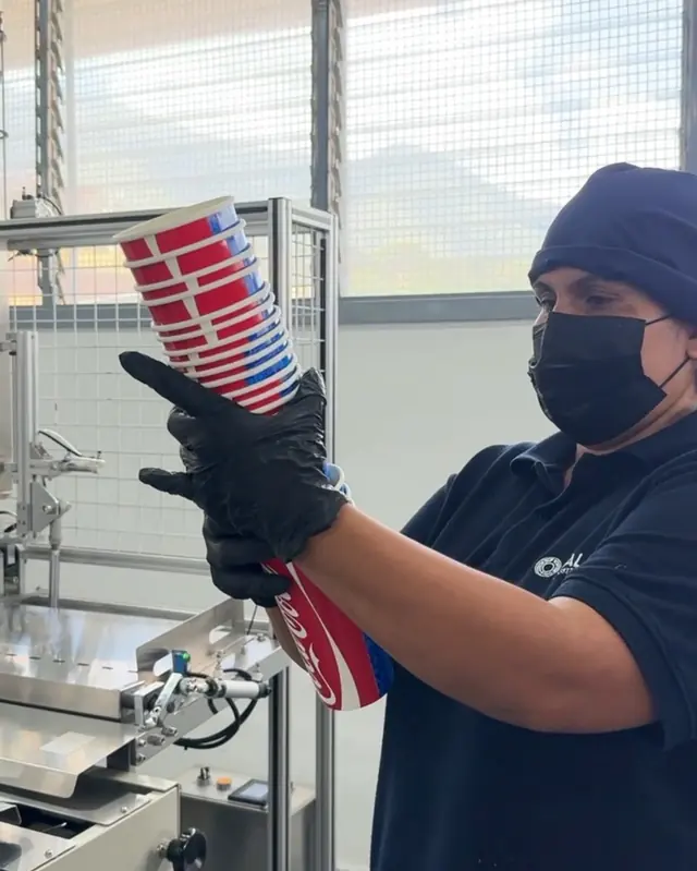 Operaria de MALPA con guantes revisando una pila de vasos impresos junto a la máquina